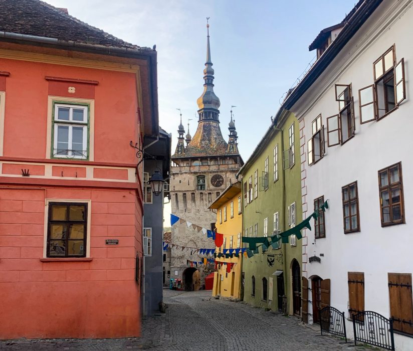 Discover Transylvania, Transylvania, Sighisoara, colorful houses, clock tower, clock, windows, doors, cobblestone street, sky, day trips from Sibiu, street flags