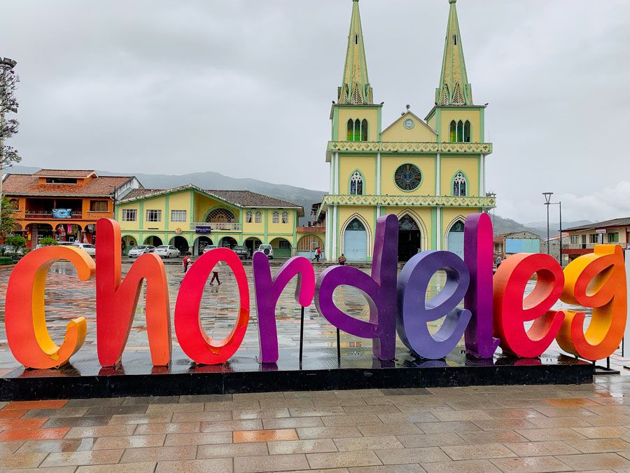 Rainbow colored Chordeleg Sign, Church, Plaza, day trips from Cuenca, Ecuador, sky, bright buildings, Cuenca day trips