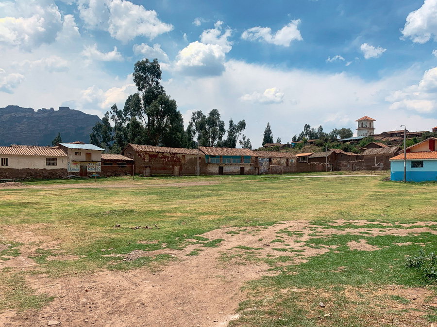 Huayqui plaza, houses, grass plaza, church, trees, mountains, clouds, sky, end of Waqrapukara trek