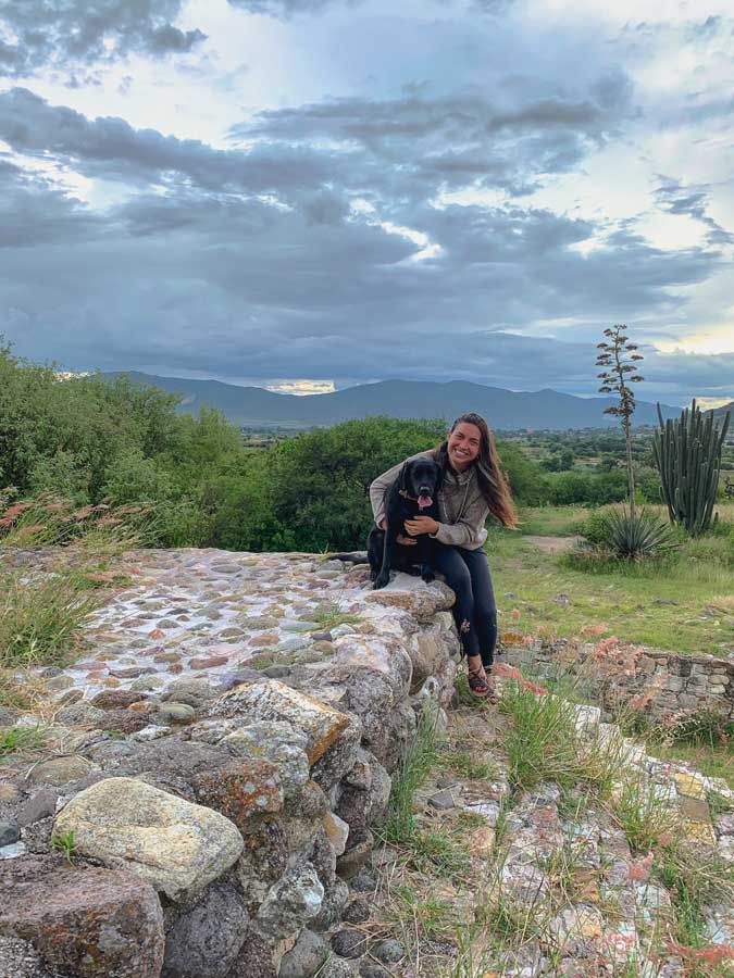 Dainzu ruins, free ruins in Oaxaca, best places to visit in Oaxaca State, Oaxaca valley, stones, grass, mountains, sky, clouds, woman, dog