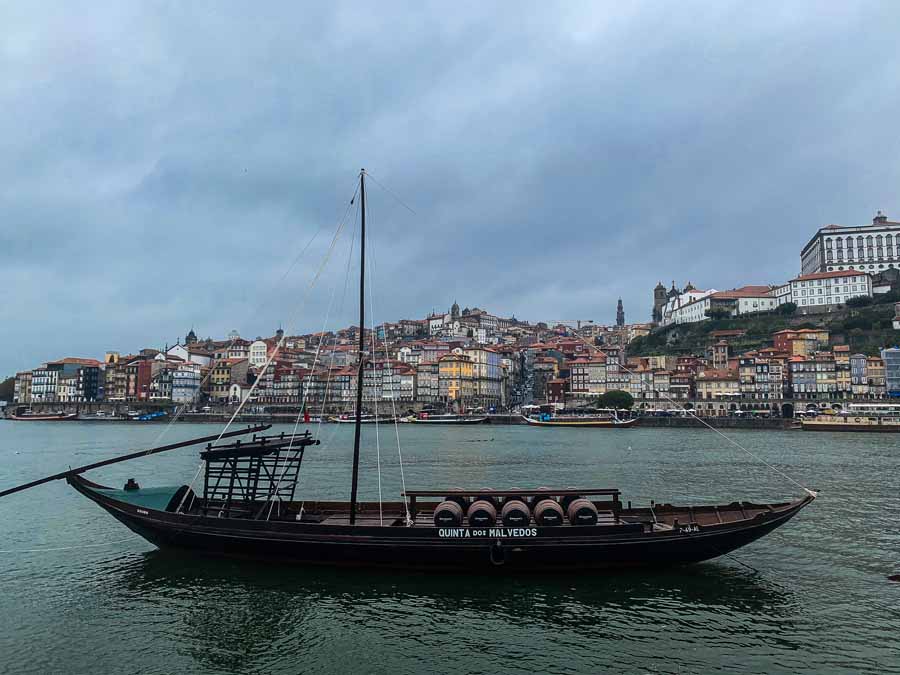 a model boat carrying barrels sits in the Rio Douro with cloudy sky above Porto in the backdrop