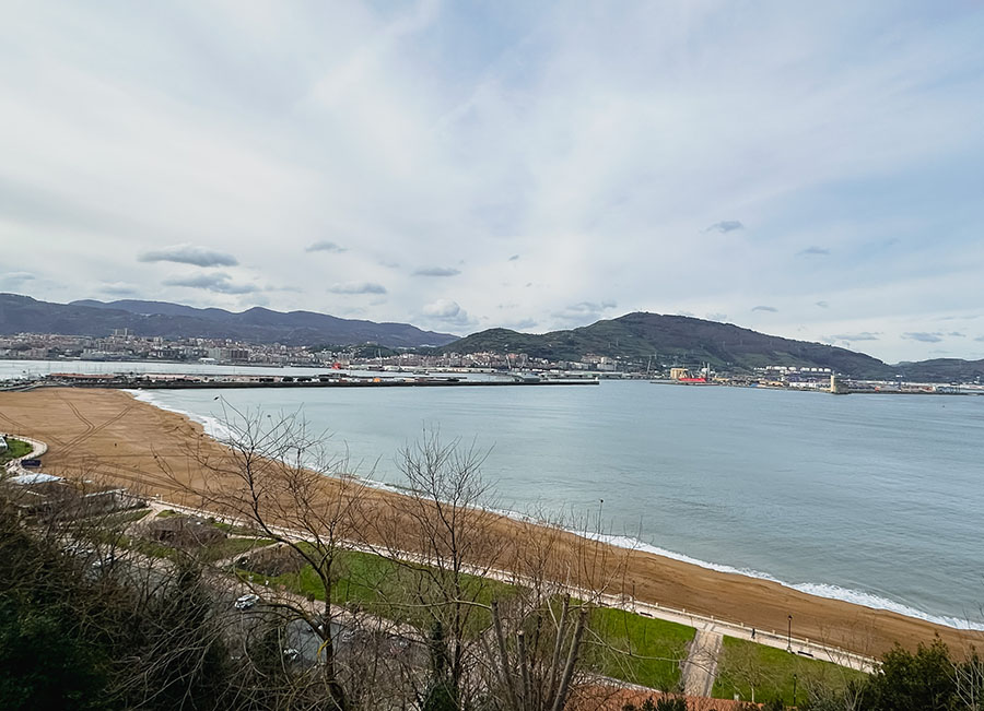 a view of a sandy beach and the large Ria de Bilbao with industrial and residential buildings