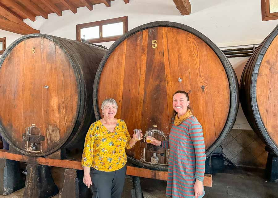 two smiling women stand in front of a large wooden barrel filled with cider in the Basque Region in Spain